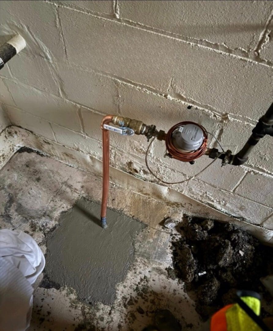 Newly installed water meter and piping against a cement wall.
