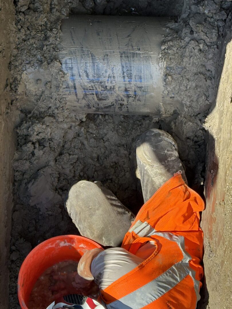 Person in orange gloves digging in dark soil with a red bucket.