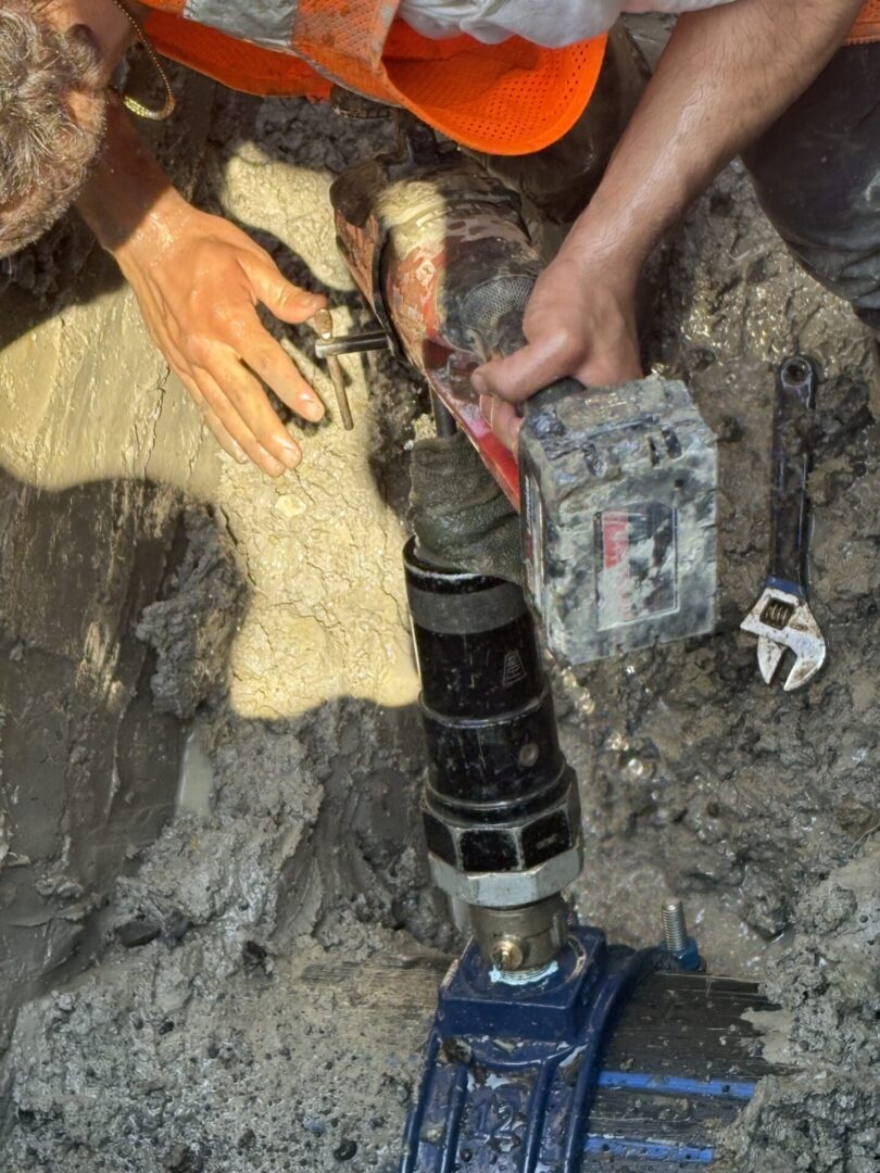 Hands working on a mechanical pipe joint underground.