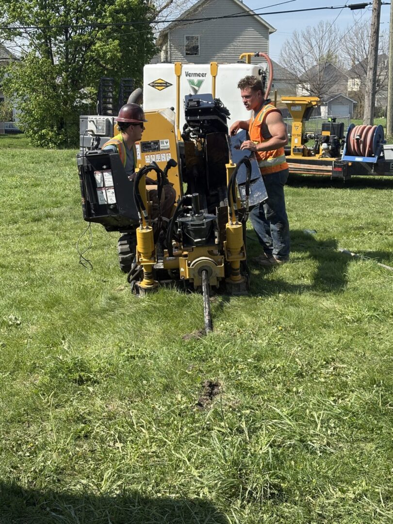 Workers operating a horizontal directional drilling machine on a grassy field.