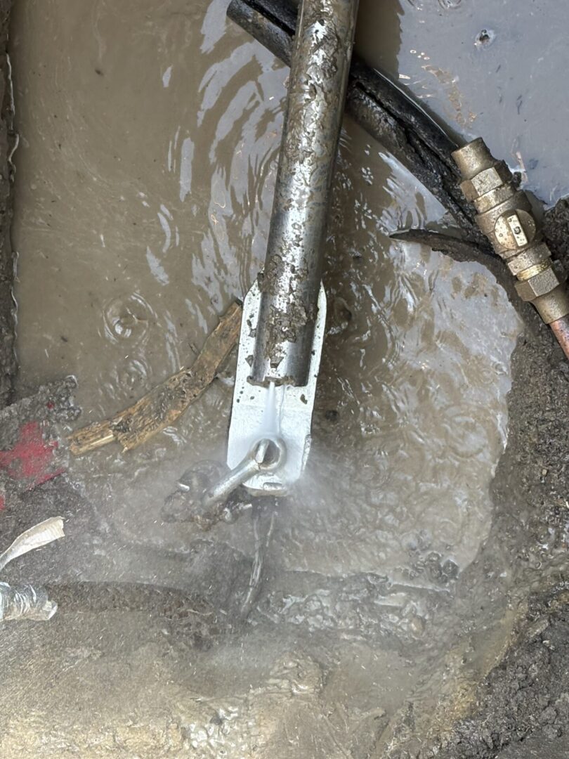 A metal tool submerged in muddy water near a hose.