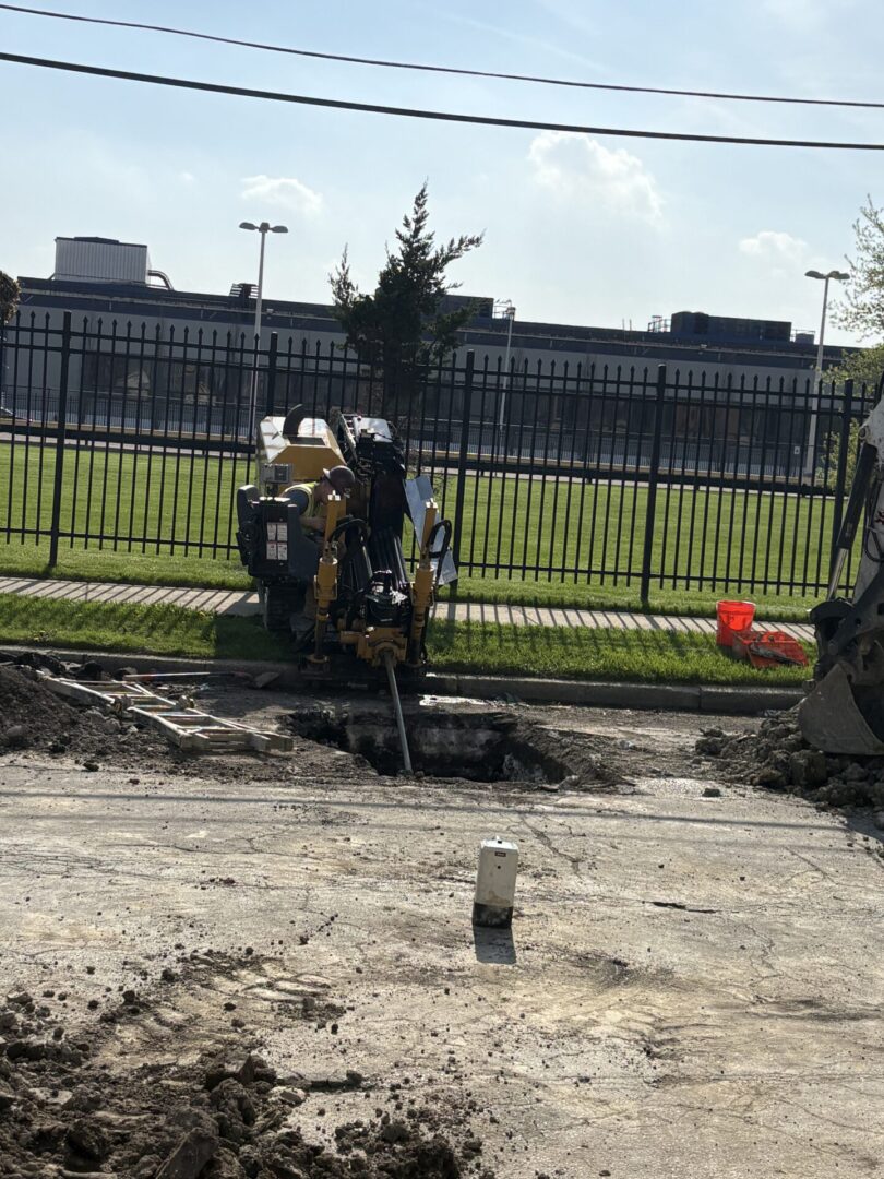 Worker using jackhammer on construction site near fence.