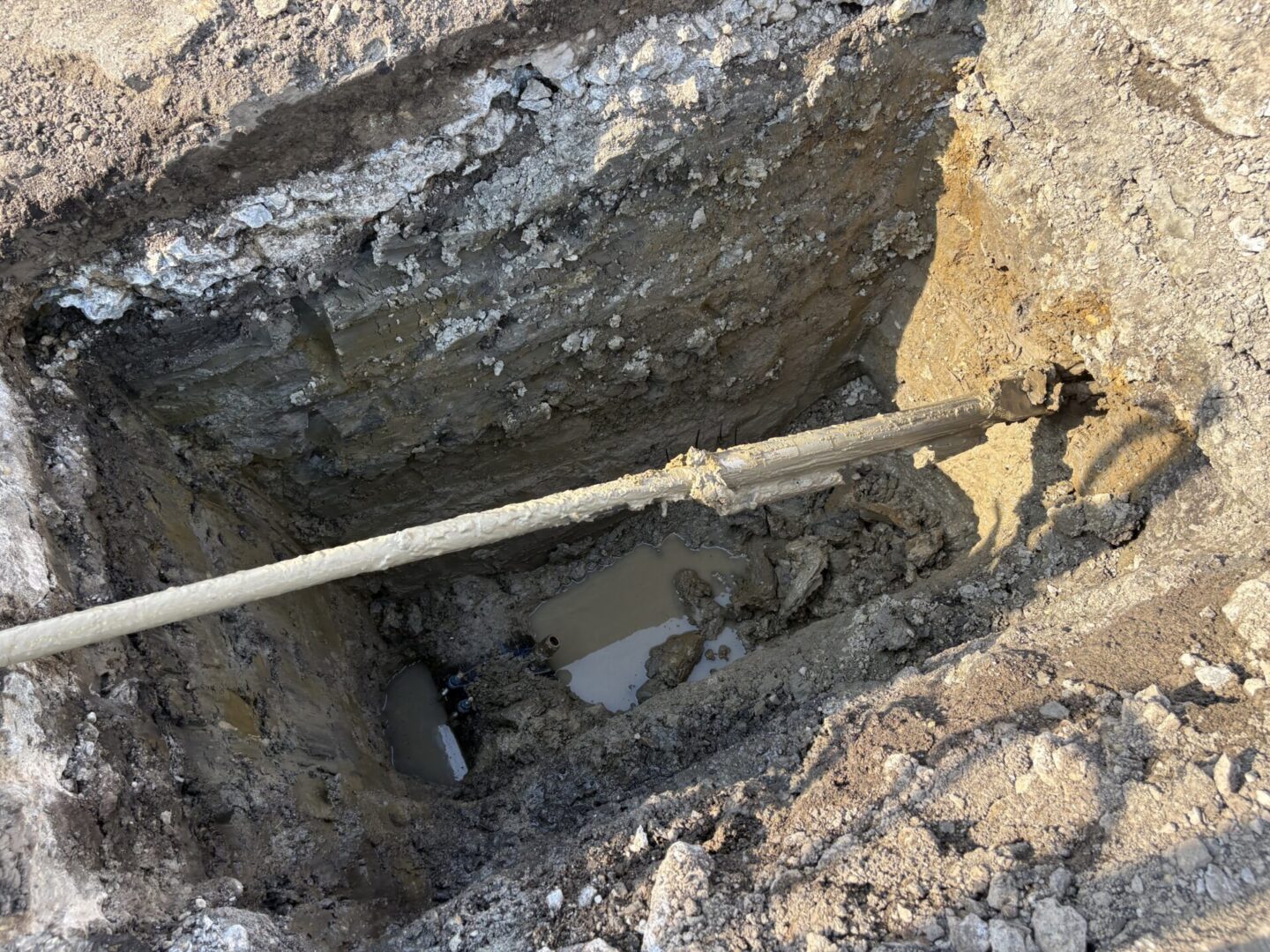 Excavation site revealing underground pipes and muddy water.