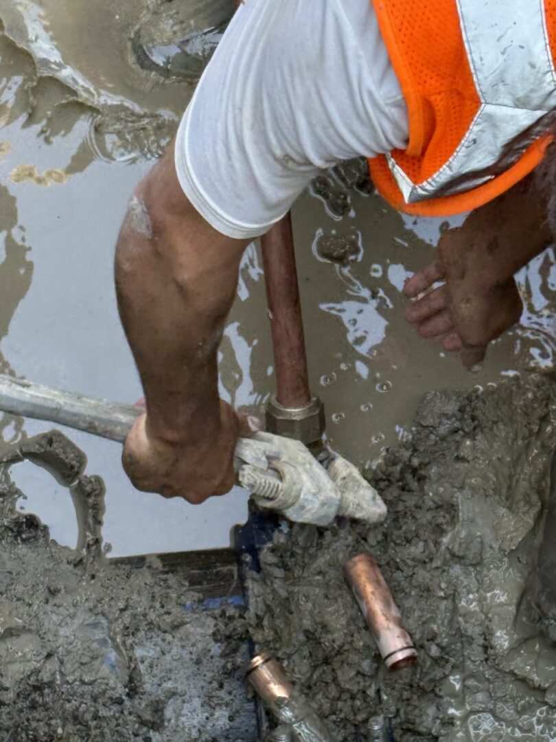 Worker repairing a leaking pipe in muddy water.