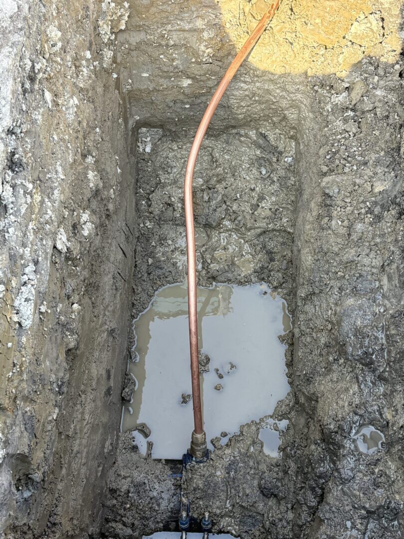 A trench with a copper pipe and water pooling inside.