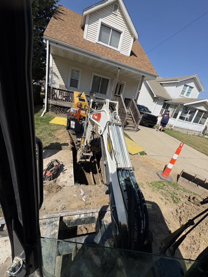 Excavator digging a trench beside a house on a sunny day.