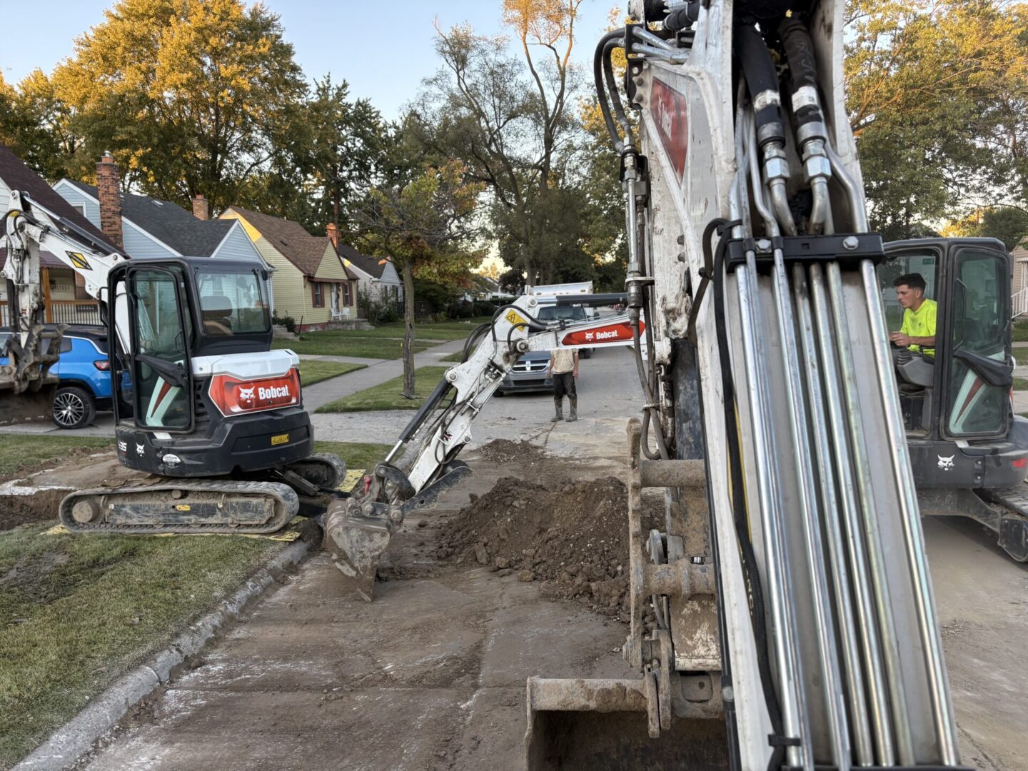 Excavator digging a trench on a residential street during daytime.