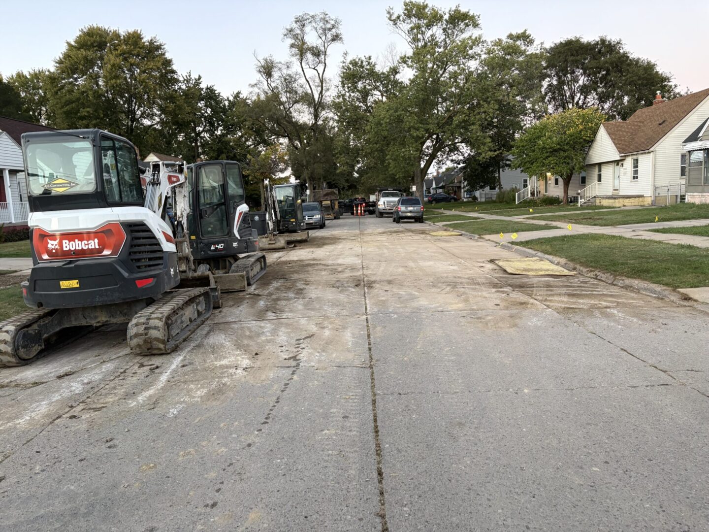 Street under construction with heavy machinery and tree-lined sides.