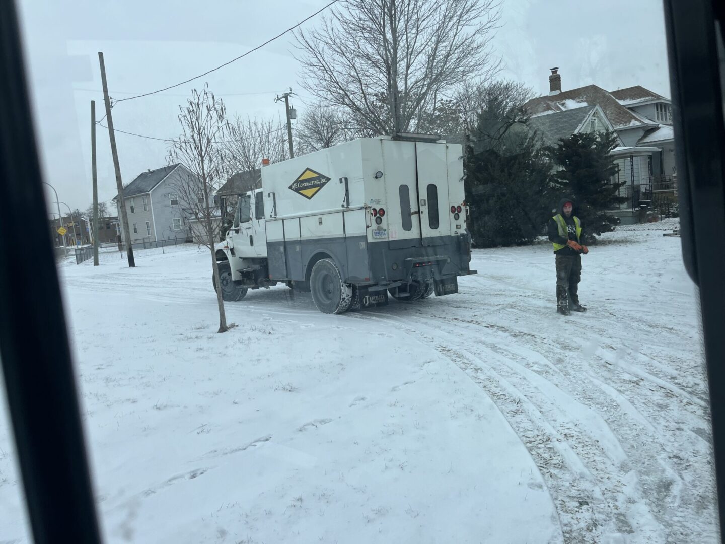 A person stands near a snow-covered road with a utility truck in the background.
