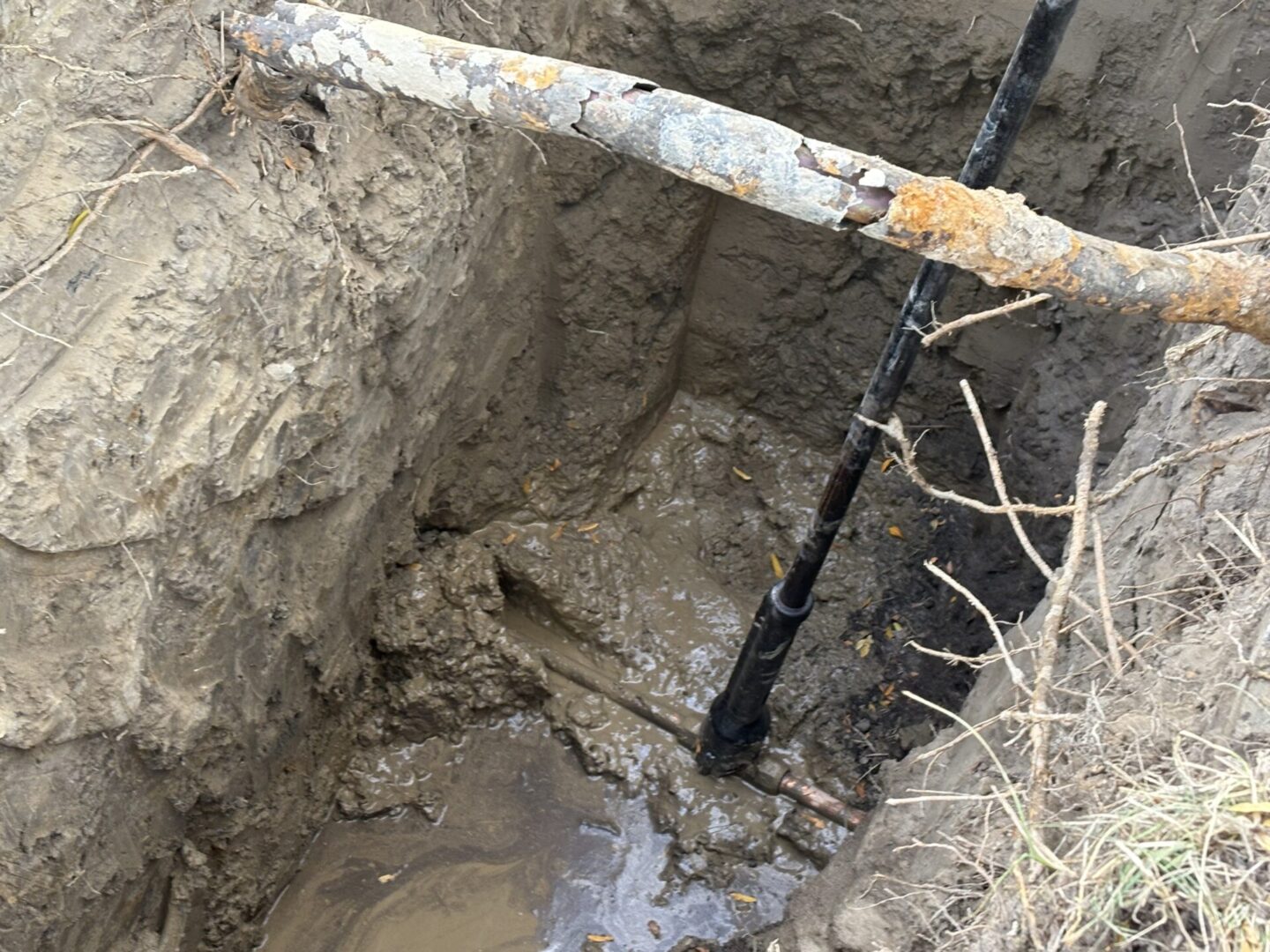 Excavation site showing muddy ground and a vertical pipe installation.