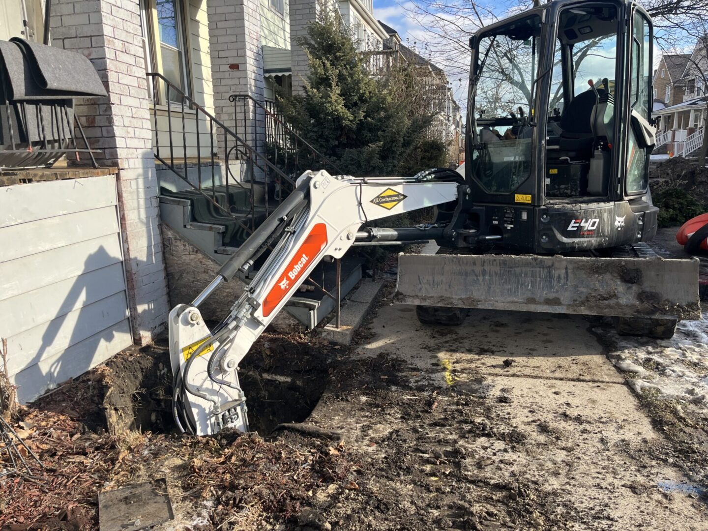 Small excavator digging near a brick building on a clear day.