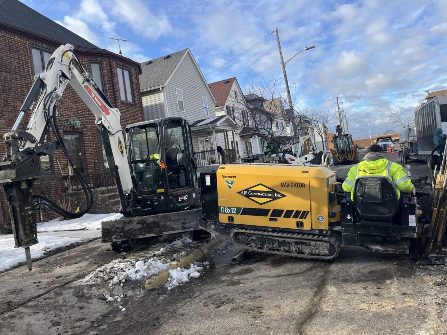 Workers operating heavy machinery on a snowy residential street.