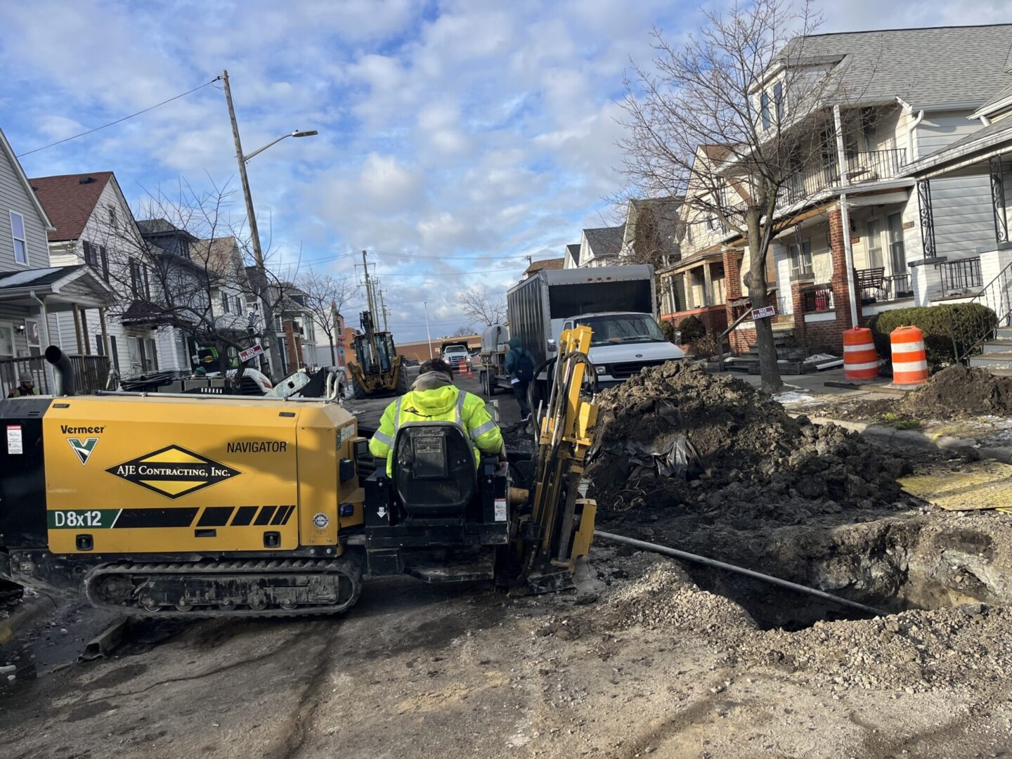 Construction workers operating excavator on a residential street.