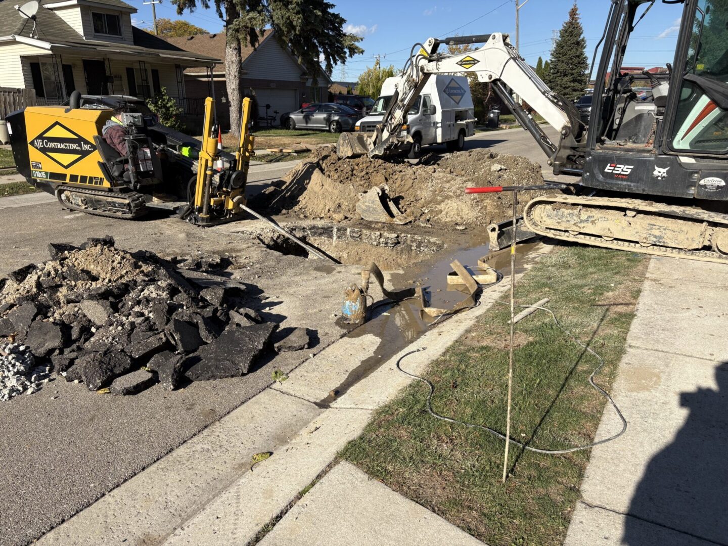 Construction work with excavator digging near a sidewalk in a residential area.
