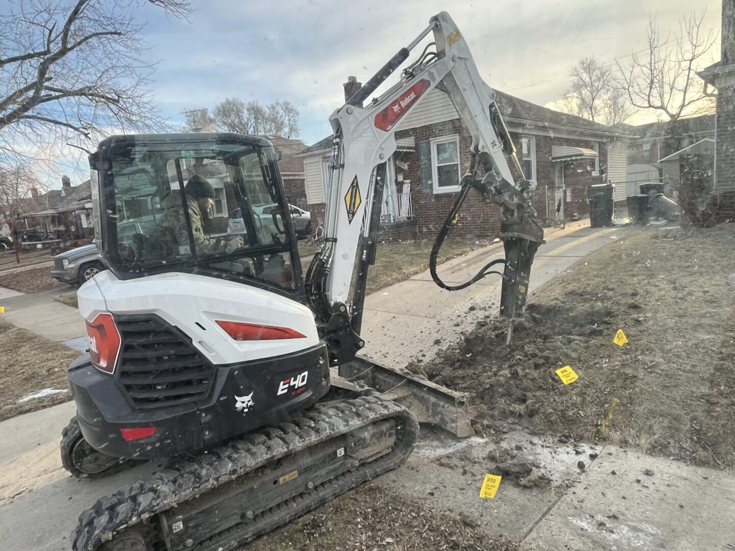 Excavator digging in a residential area with marked spots on the ground.