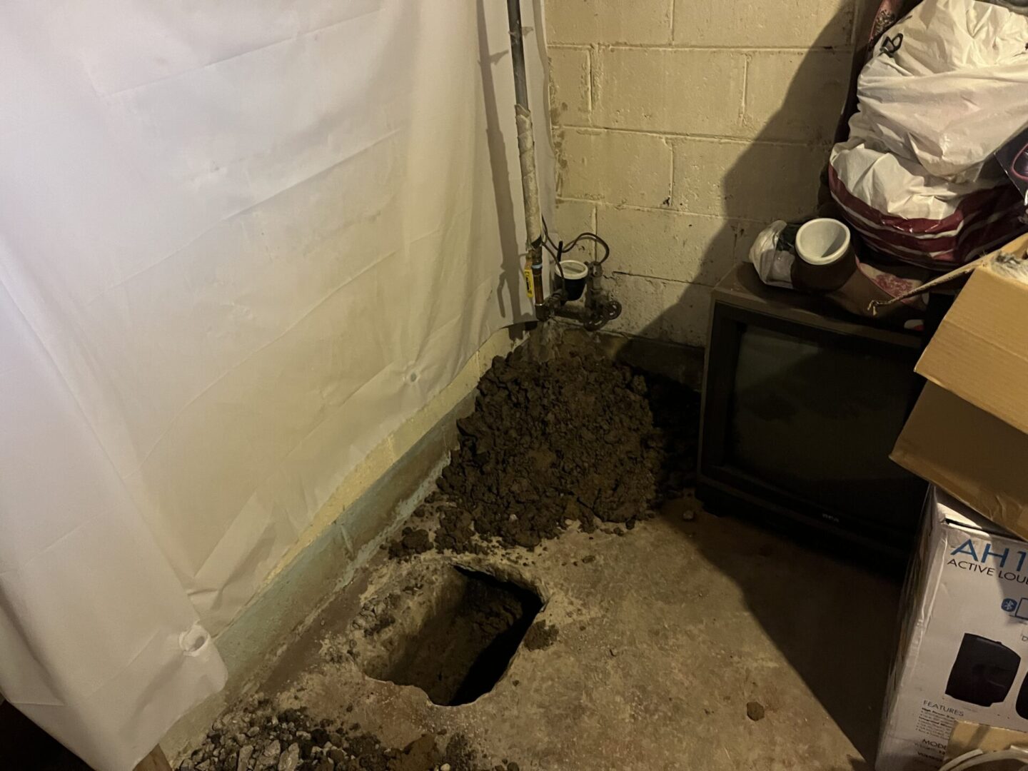 A hole dug in a basement floor with a pile of dirt next to it.