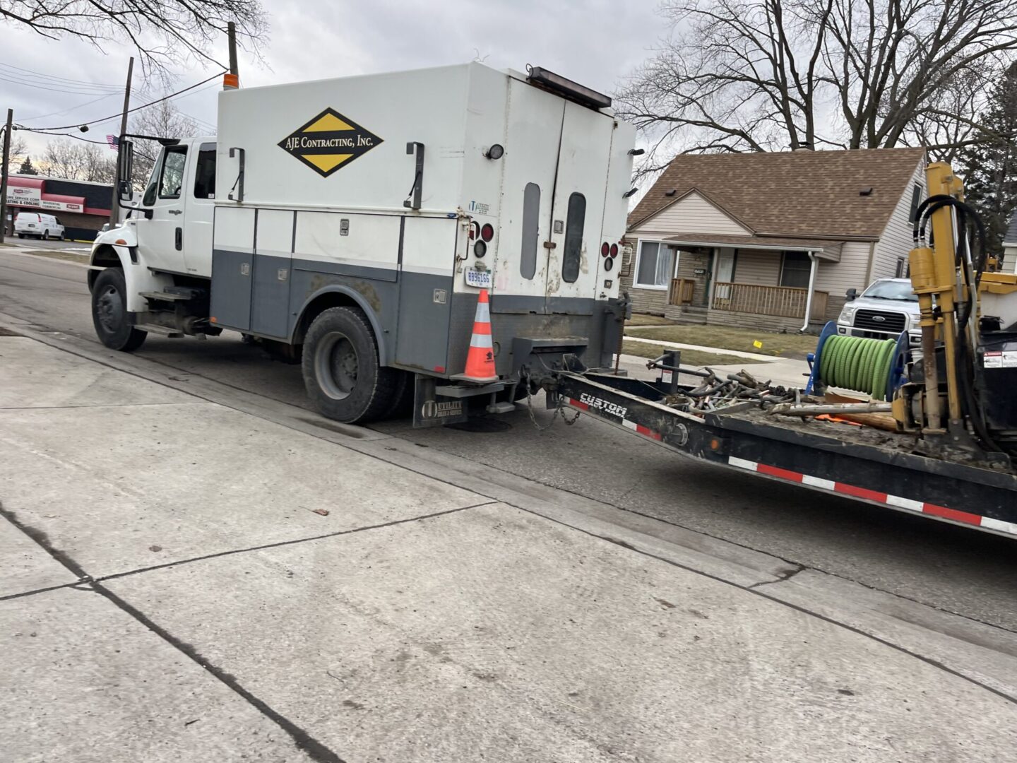 White utility truck with trailer loaded with wooden pallets parked on street.