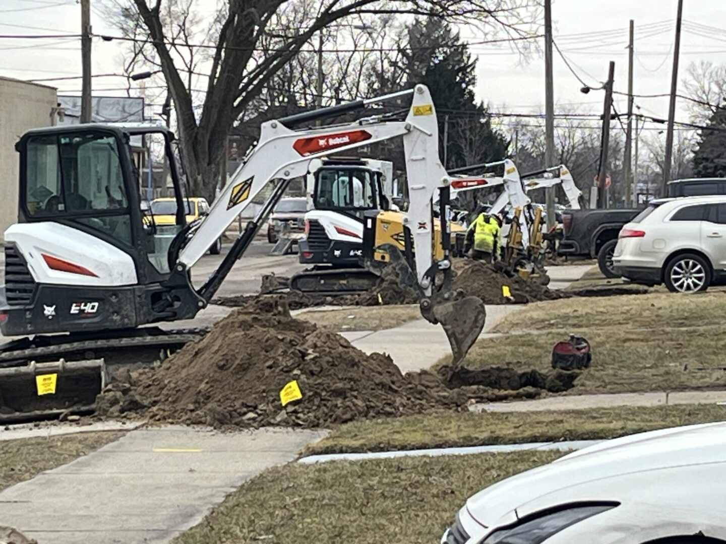Workers operate excavators on a muddy construction site near a sidewalk.