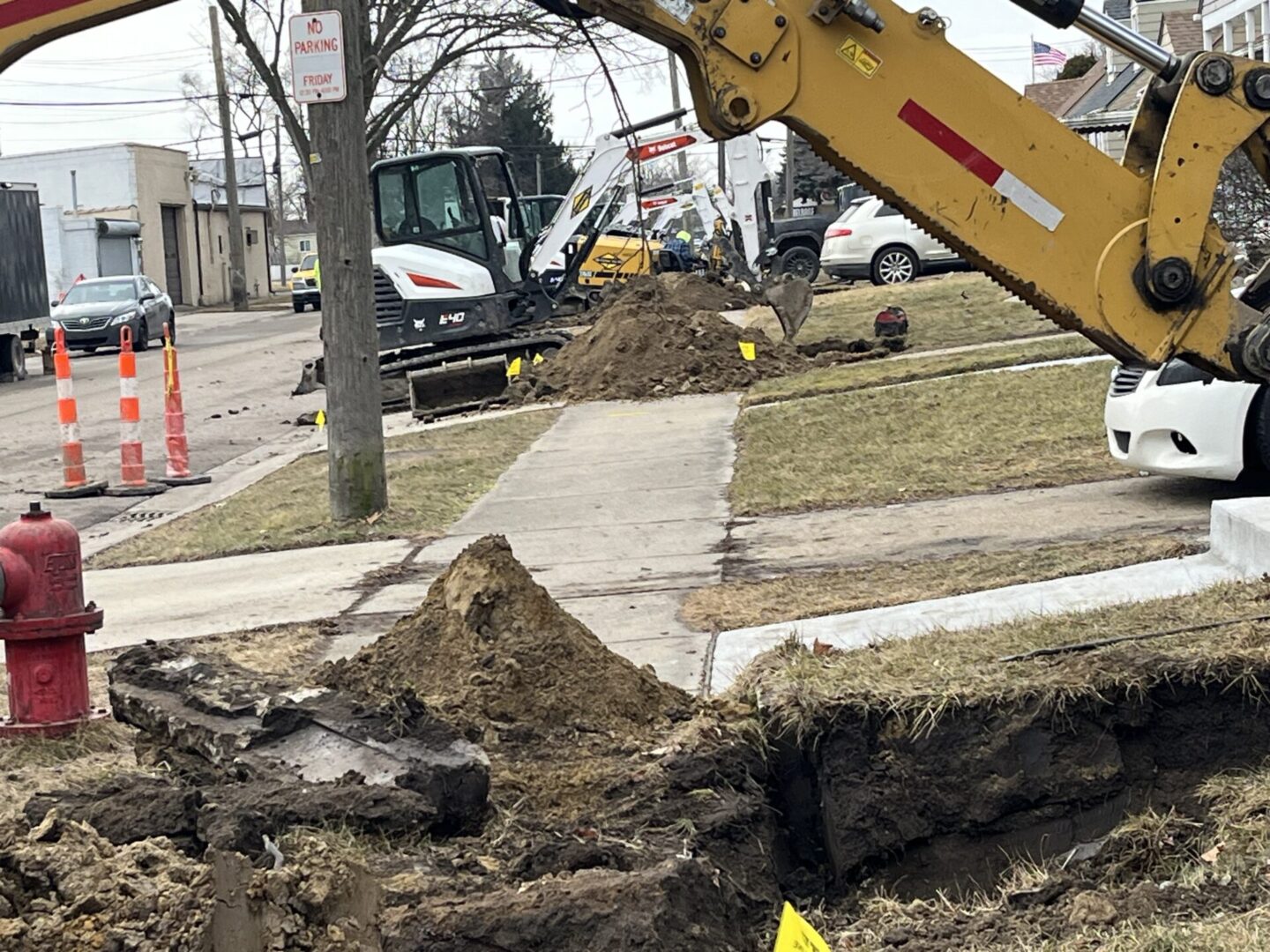 Excavator digging a trench along a suburban sidewalk in winter.