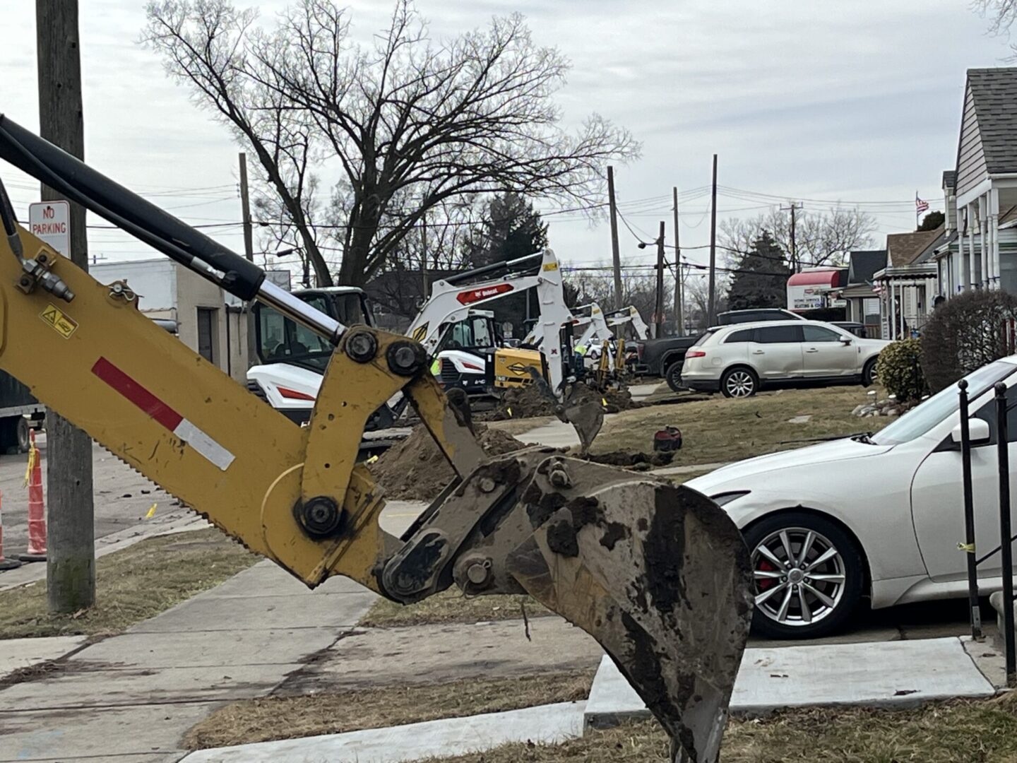 Excavator bucket resting on a concrete surface near parked cars on a cloudy day.