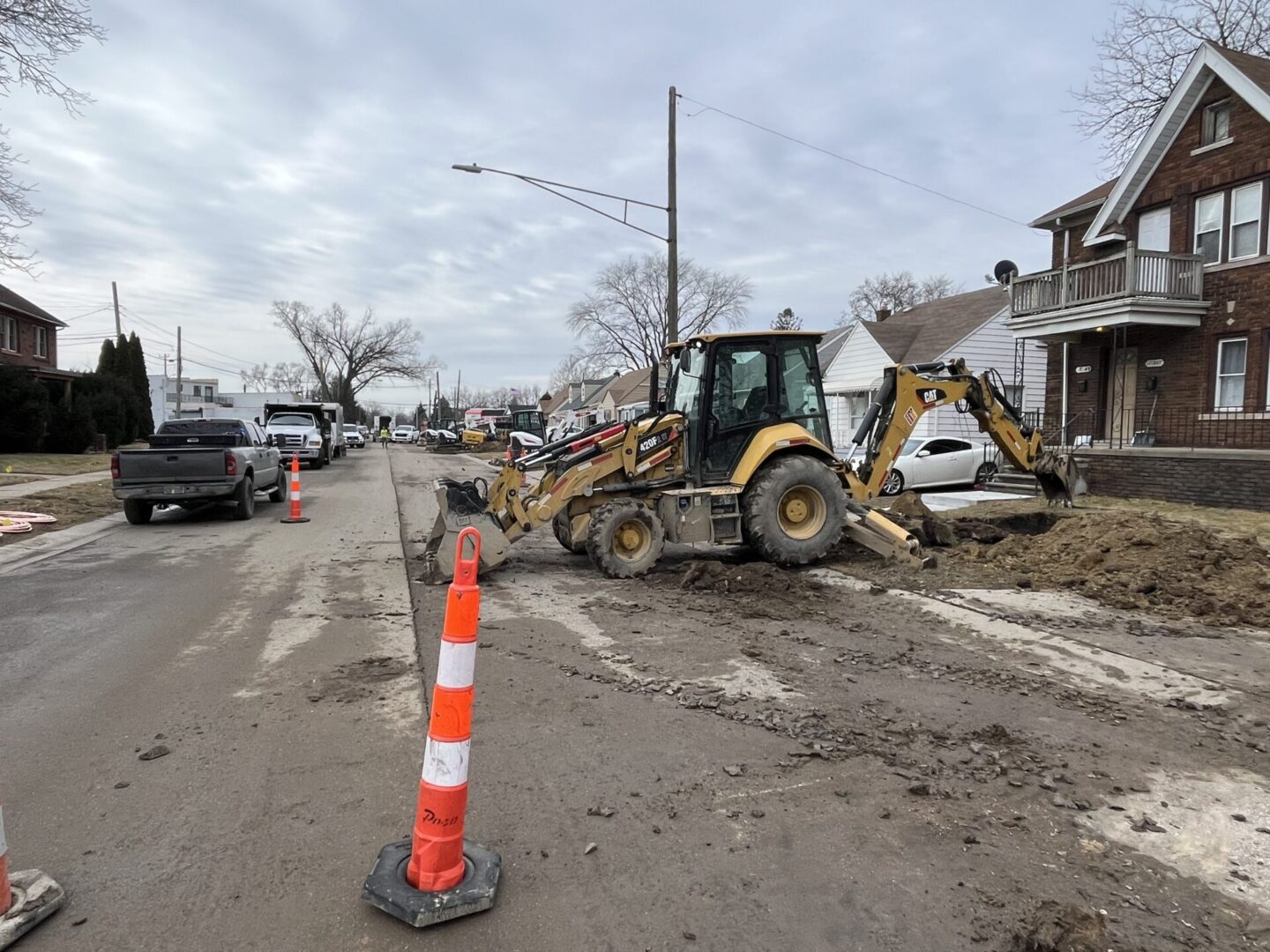Construction equipment working on a muddy street beside a traffic cone.