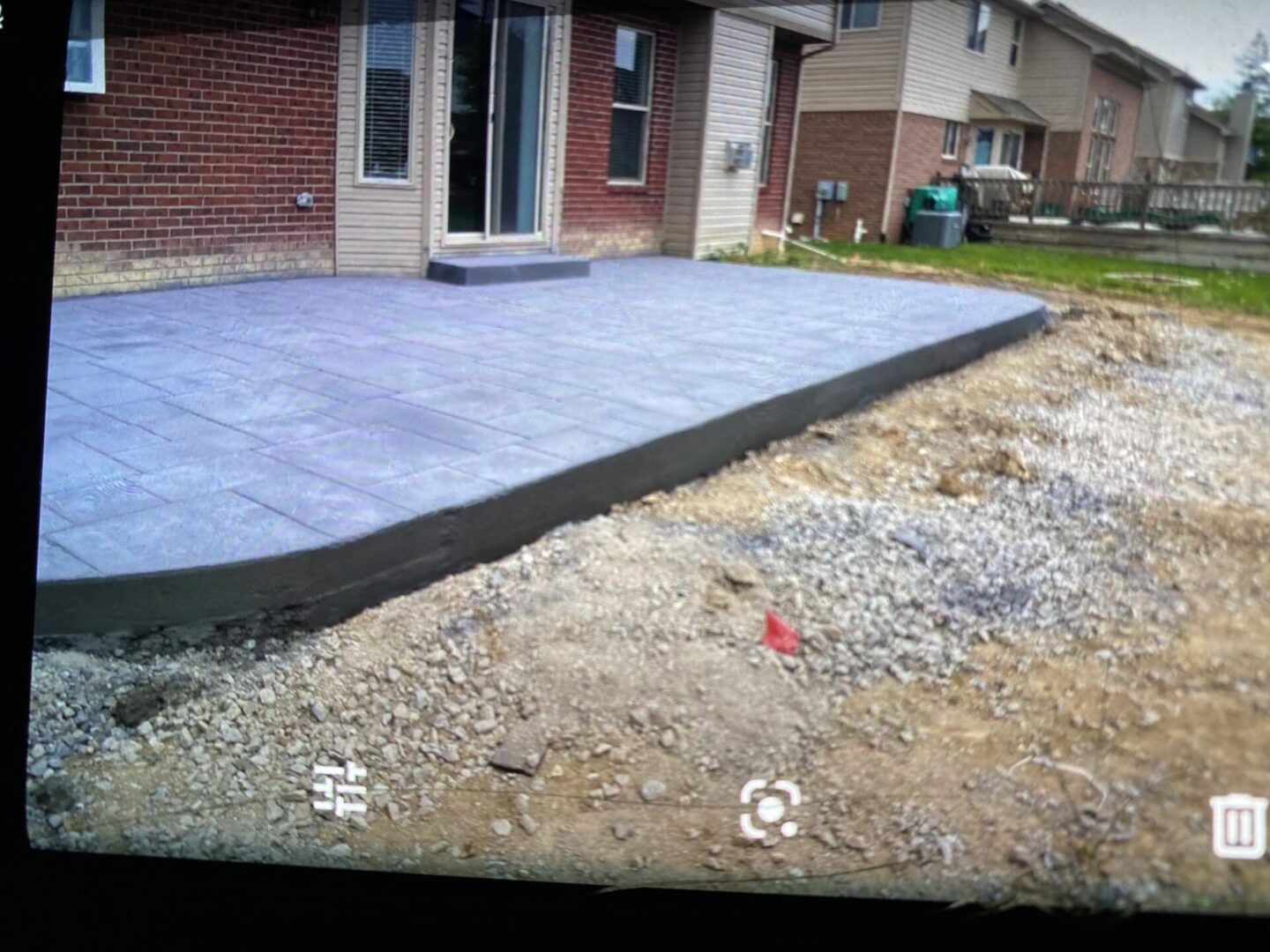 Newly poured concrete patio next to a house with gravel surrounding it.
