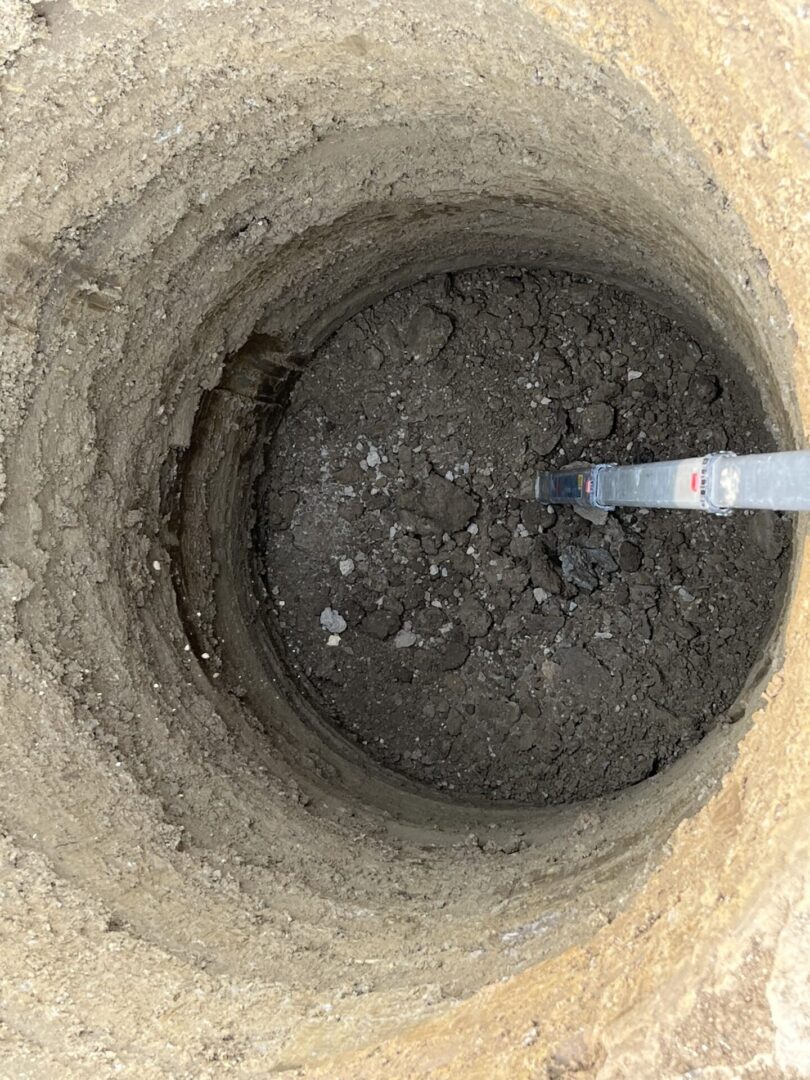 A deep hole dug in the ground with a metal rod inside.