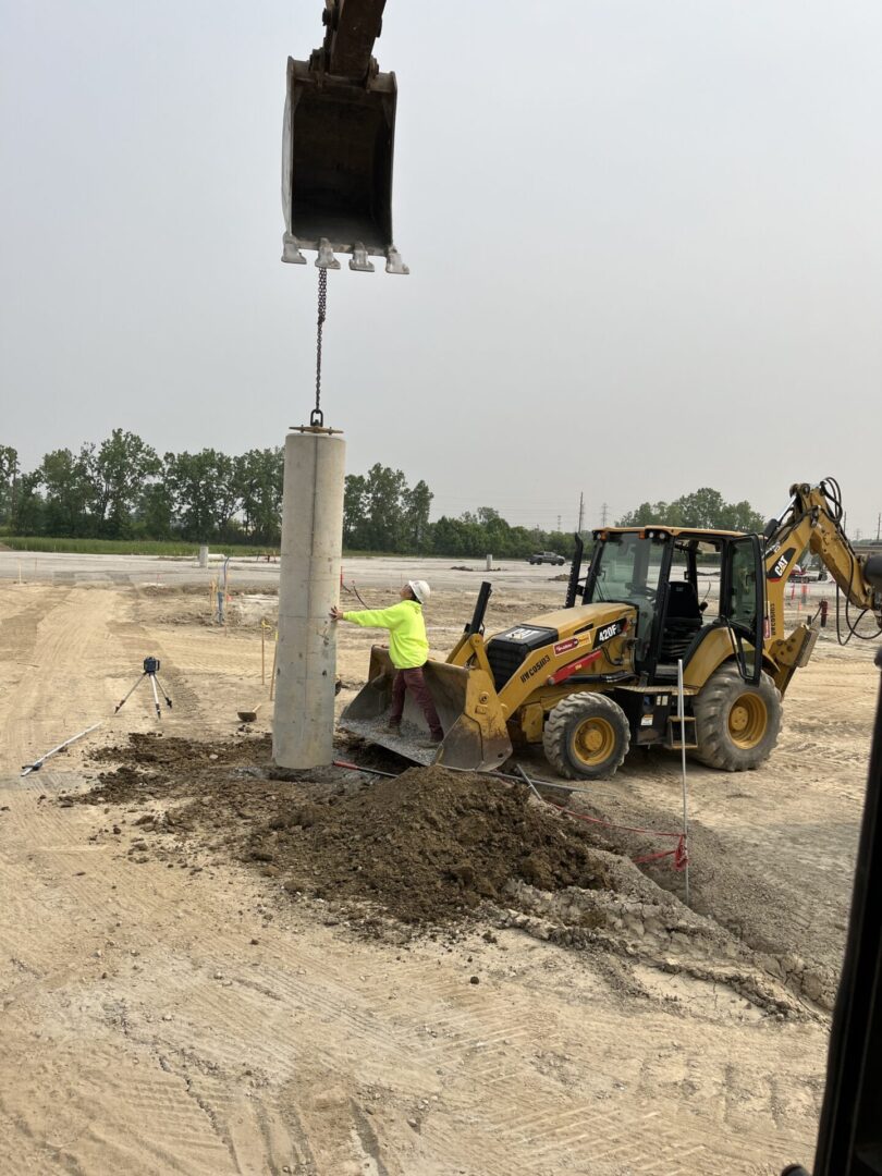 A backhoe loader digging near a concrete pillar in a dry, open area.