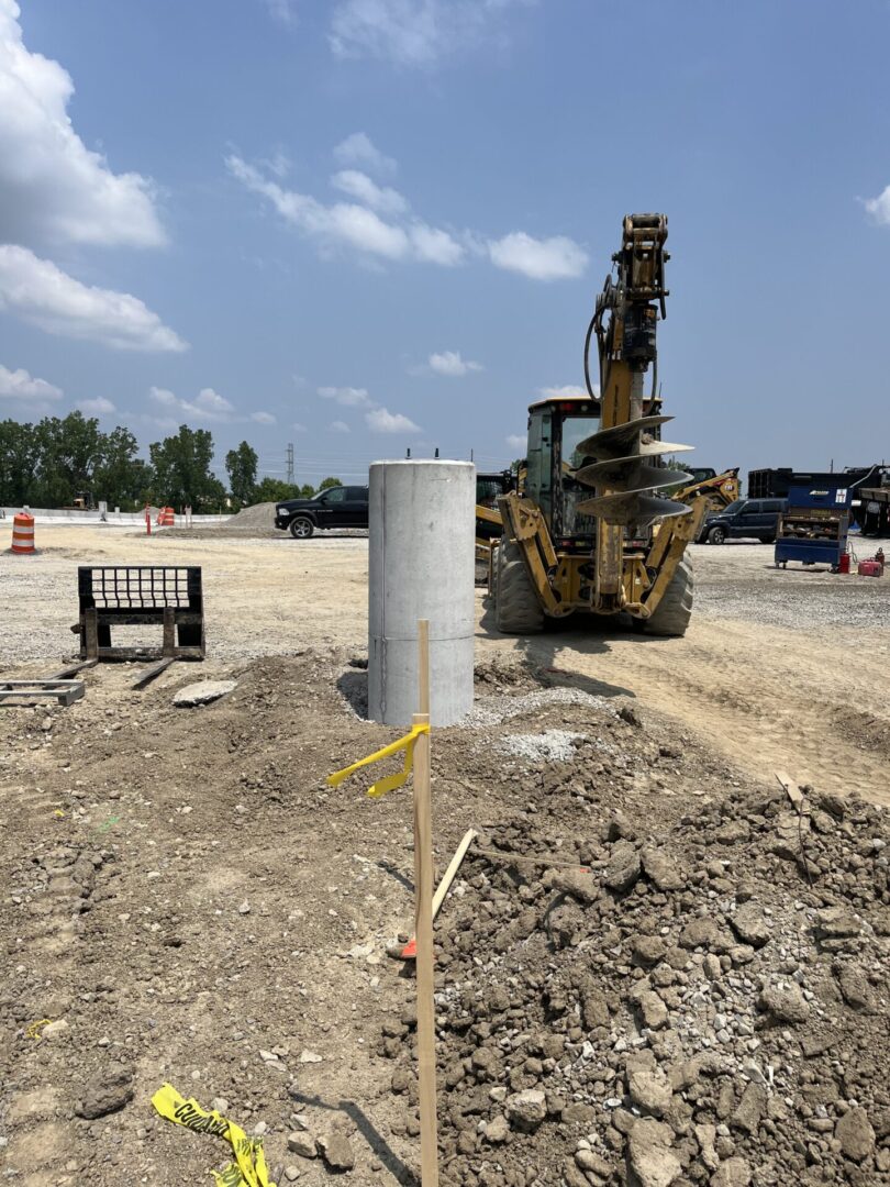 Construction site with heavy machinery and a trench marked by a wooden stake.