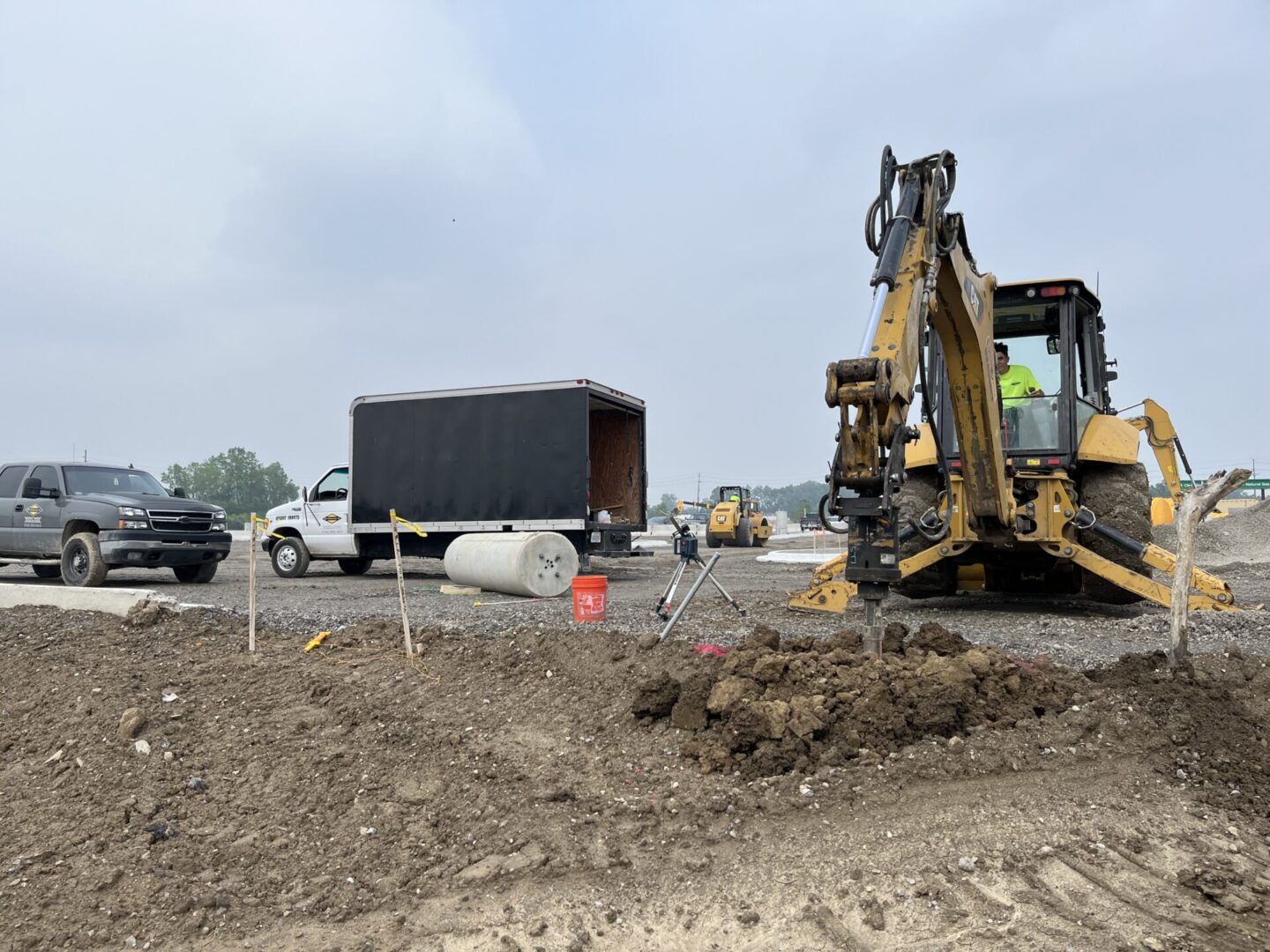 Construction site with excavator and truck under a cloudy sky.