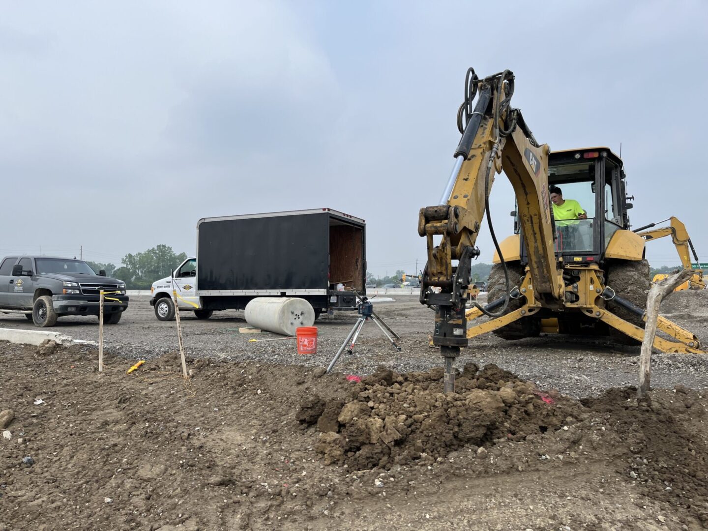 Construction site with excavator digging near a truck and road.