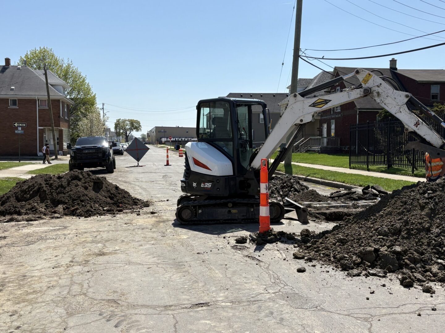 Excavator digging on residential street with cones