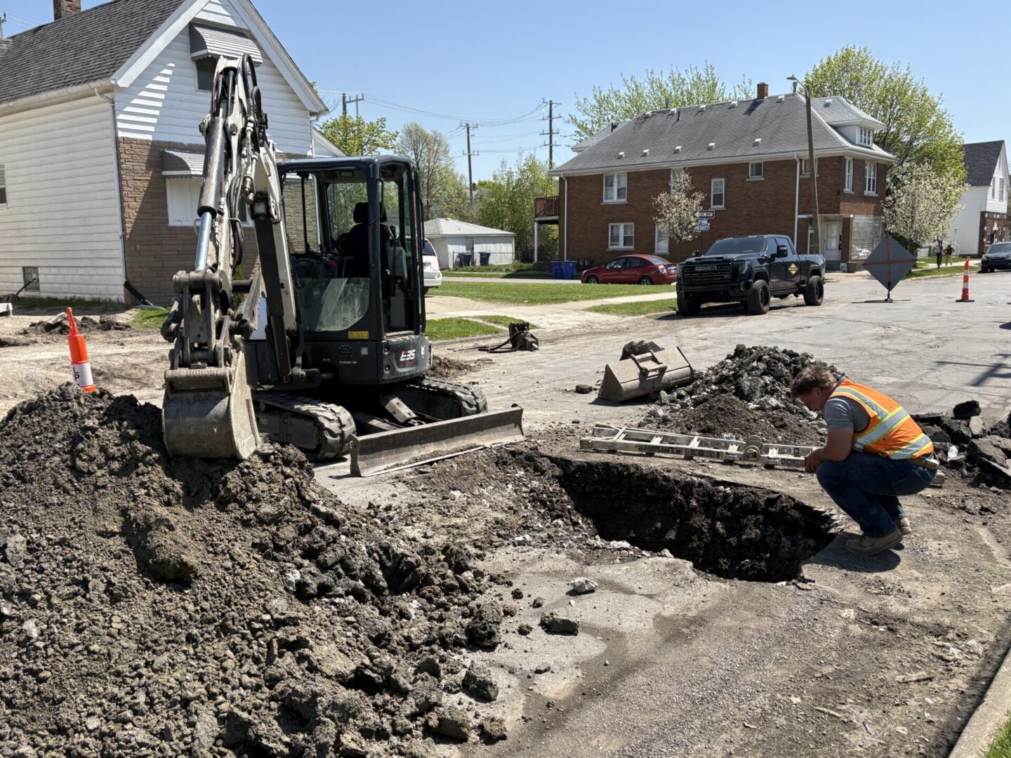 Worker inspecting hole beside excavator on street