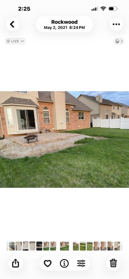 Backyard with a stone patio, picnic table, and green lawn beside a brick house.