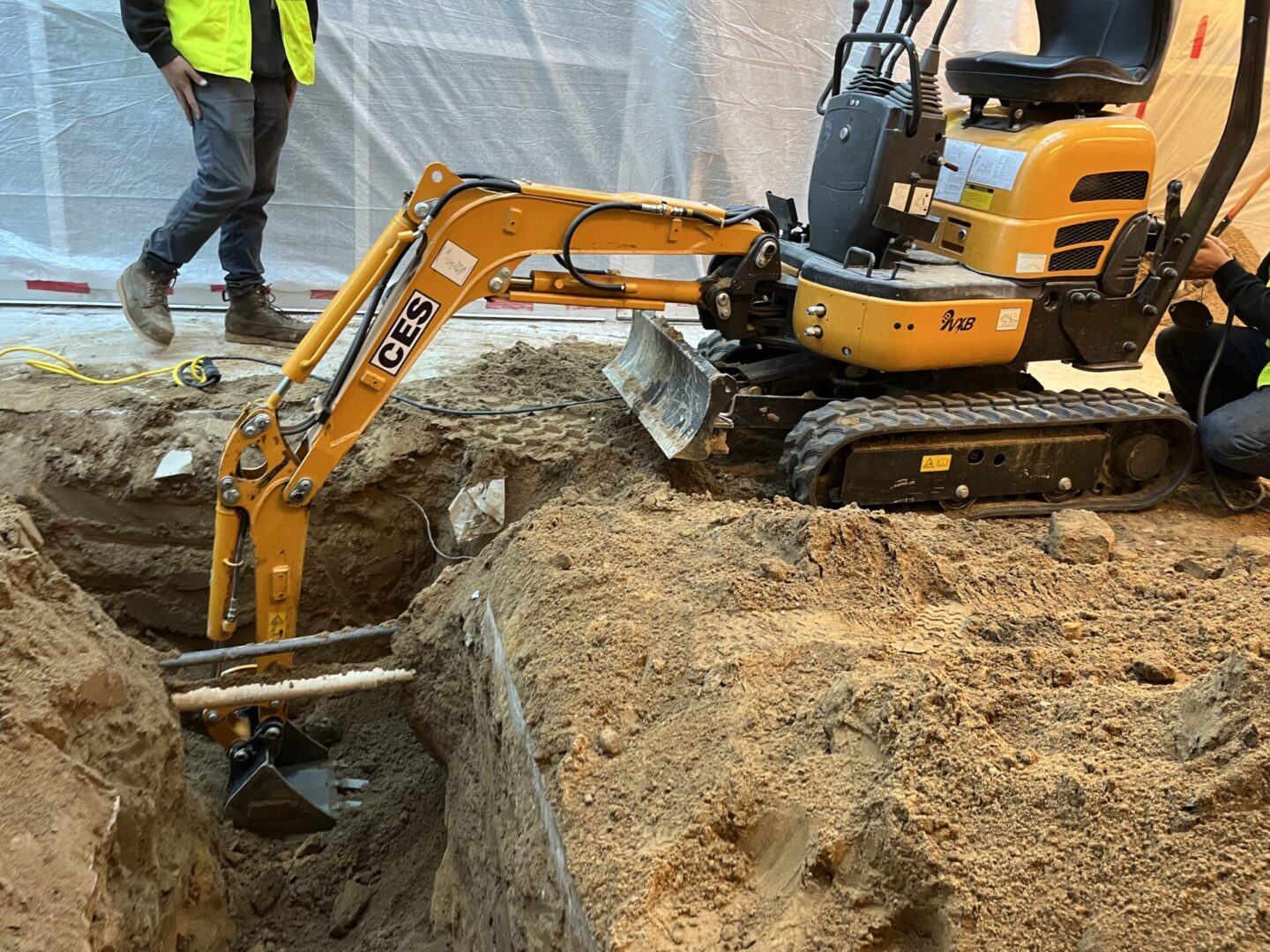 A yellow mini excavator digging dirt at a construction site.