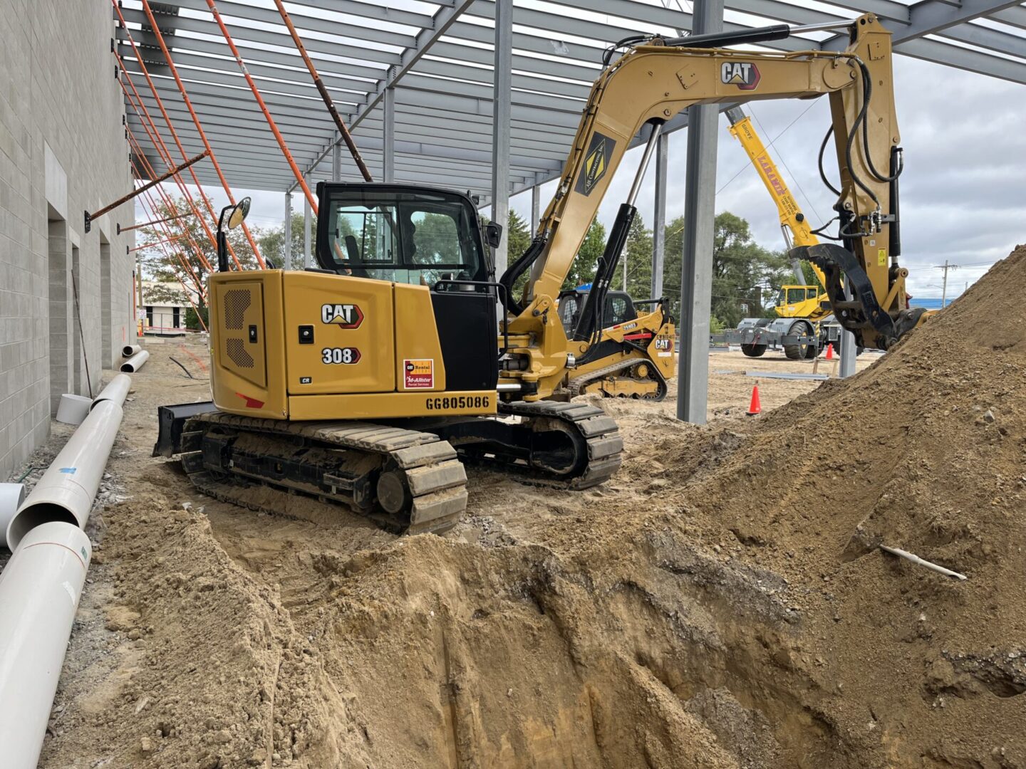 Mini excavator digging a trench inside a greenhouse structure.