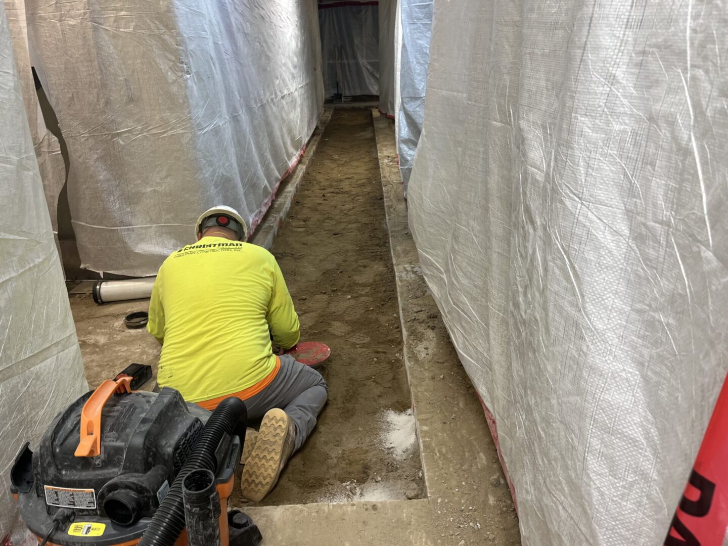 Worker kneeling on the ground in a narrow construction area.