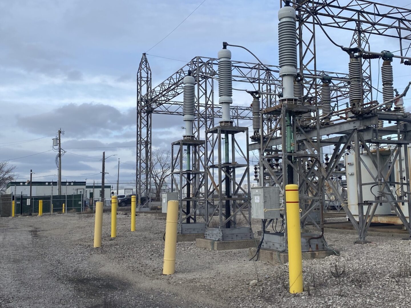 Electrical substation with steel structures and yellow safety poles under a cloudy sky.