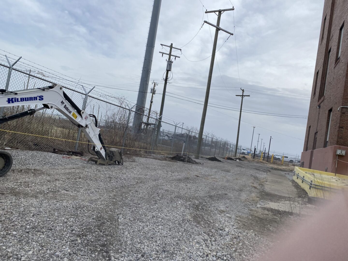 Industrial area with gravel road and utility poles under cloudy sky.