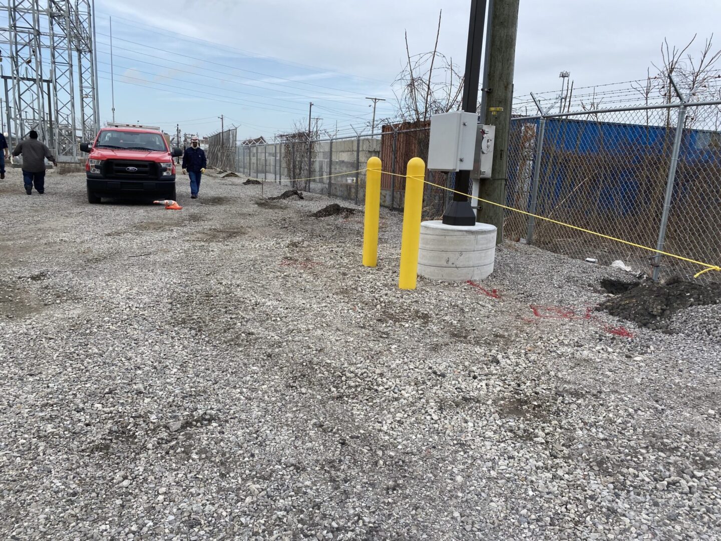 Gravel pathway with yellow bollards and a chain-link fence beside a parking area.